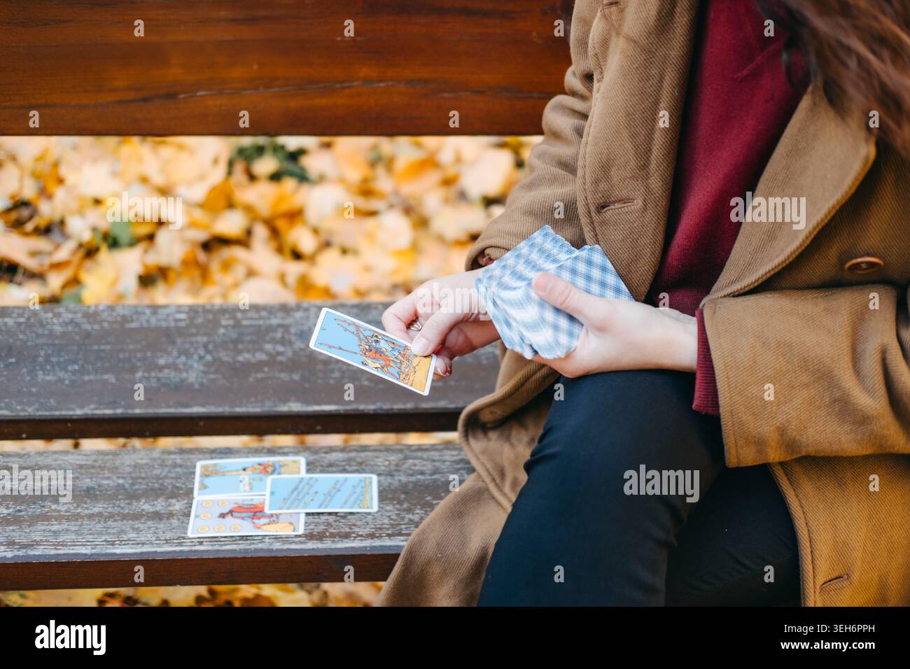 La persona siede su una panchina di legno tenendo il mazzo e la carta da disegno. Lettura di carte di Tarocchi, pratiche spirituali moderne, rituale di stile di vita esoterico. Varsavia, Polonia Foto Stock