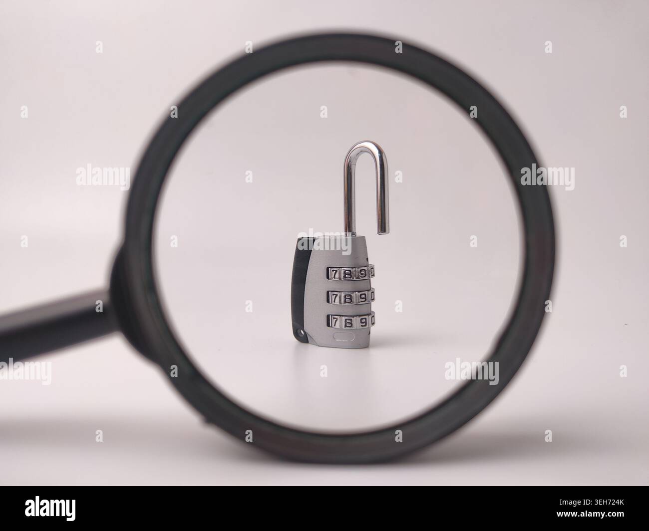 Un lucchetto a combinazione aperto in argento con quadranti numerici è incorniciato e controllato attraverso una lente di ingrandimento nera. Foto Stock