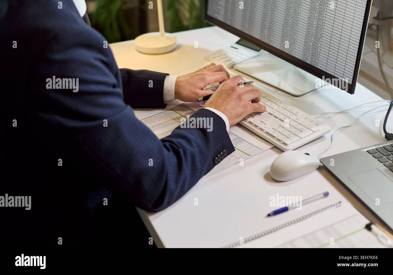 Uomo d'affari che digita i dati finanziari sulla tastiera durante l'audit contabile in ufficio Foto Stock