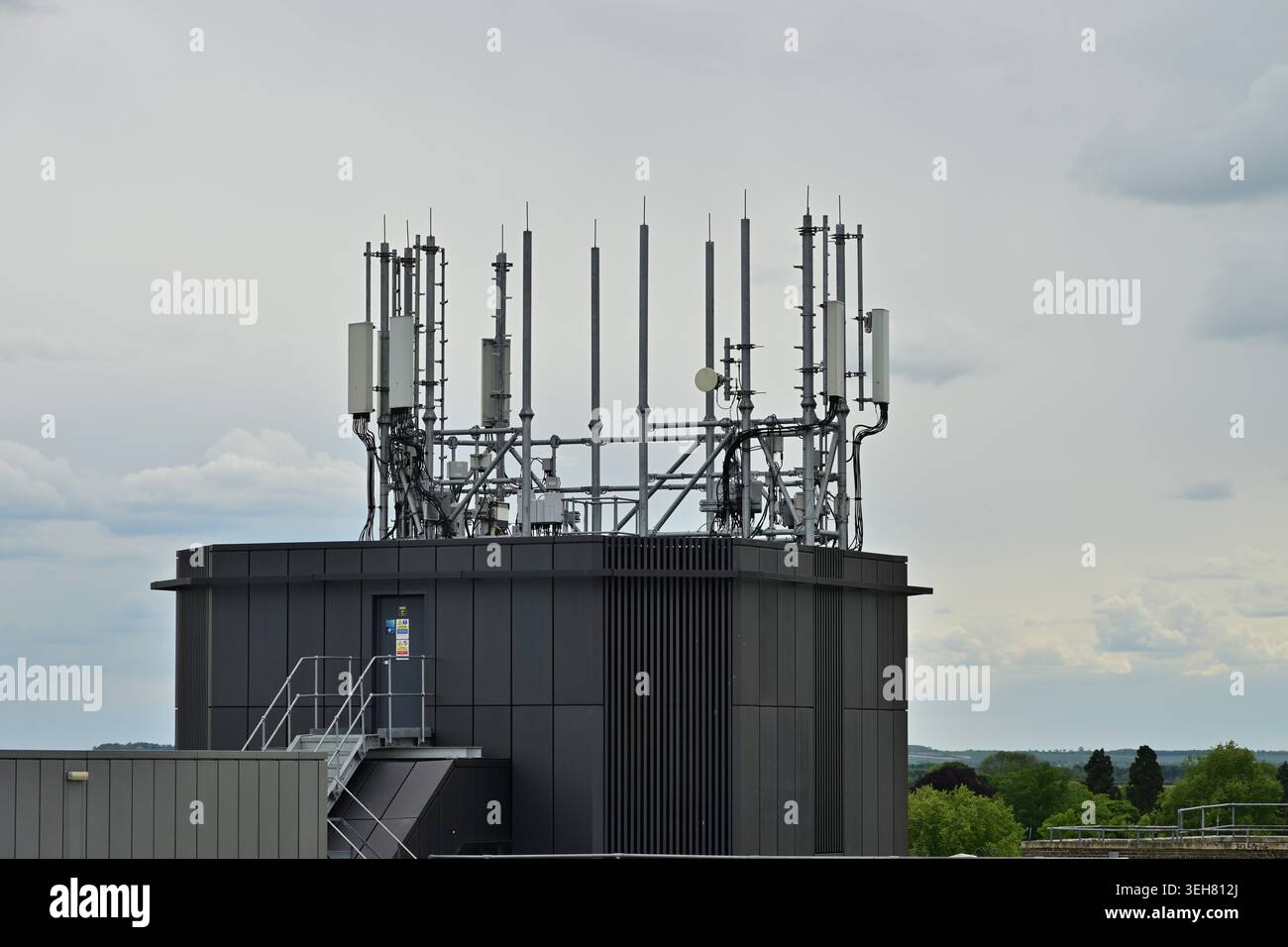Antenne e cavi cellulari sul tetto in un edificio grigio con segnali di avvertimento sotto Foto Stock