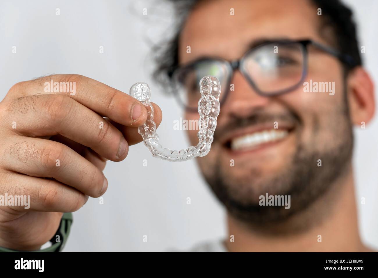 Uomo sorridente che tiene un allineatore dentale invisibile per il trattamento ortodontico Foto Stock