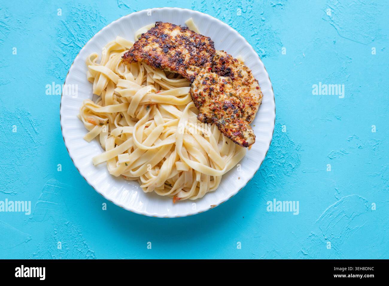 Primo piano di tagliatelle salate con pollo fritto croccante servito su un vivace sfondo blu Foto Stock