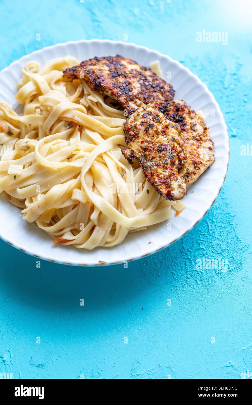 Primo piano di tagliatelle salate con pollo fritto croccante servito su un vivace sfondo blu Foto Stock