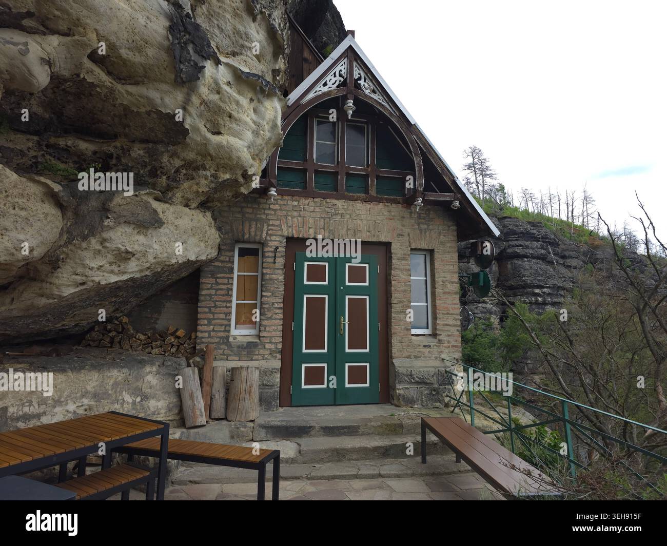 La maestosa porta Pravcice, il più grande arco naturale in pietra arenaria d'Europa, la Svizzera boema. Cottage in pietra costruito nella scogliera con porta verde, in legno Foto Stock