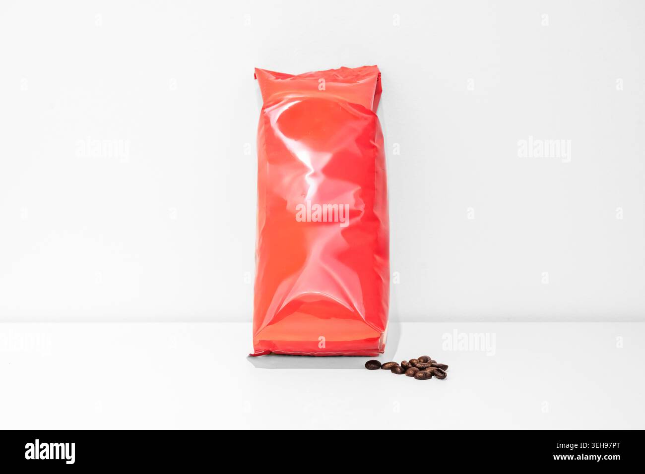 Sacchetto ermetico rosso brillante con chicchi di caffè su una superficie bianca. Foto Stock