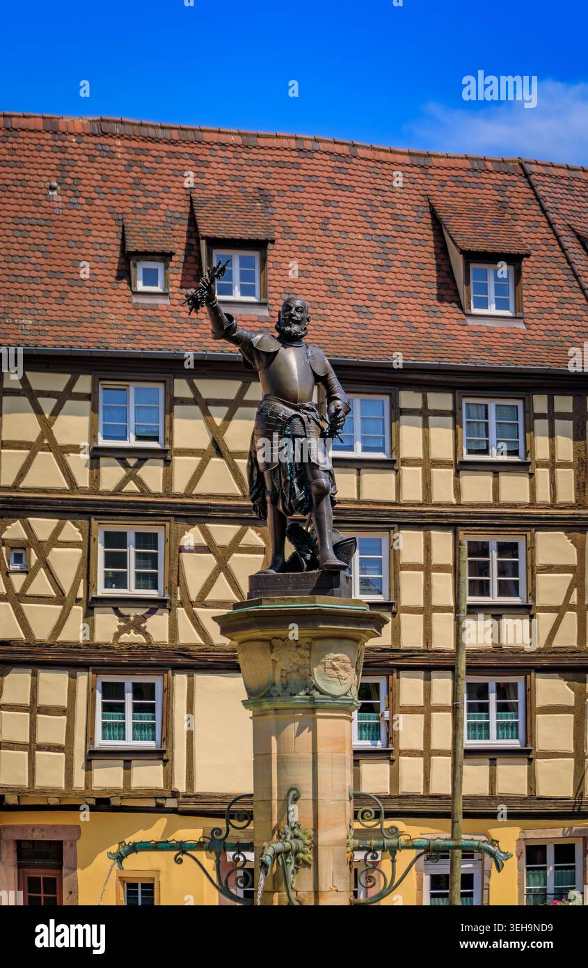 La statua del 1898 di Lazare de Schwendi che regge una vite sulla cima di una fontana storica di fronte a una tradizionale casa in legno a Colmar, in Francia Foto Stock