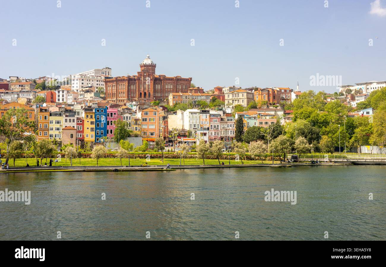STANBUL, TURCHIA - 9 MAGGIO 2026: Una vista panoramica sul lungomare dello storico quartiere Balat con vari cartelli commerciali e l'iconico Phan in mattoni rossi Foto Stock