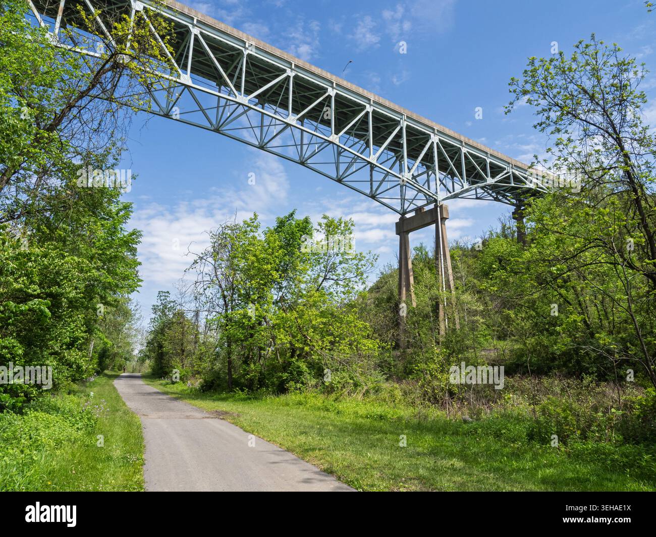 Un massiccio ponte a capriata in acciaio su Ravensburg Blvd torreggia su un percorso di ricreazione lastricato circondato da verdi boschi in Pennsylvania Foto Stock