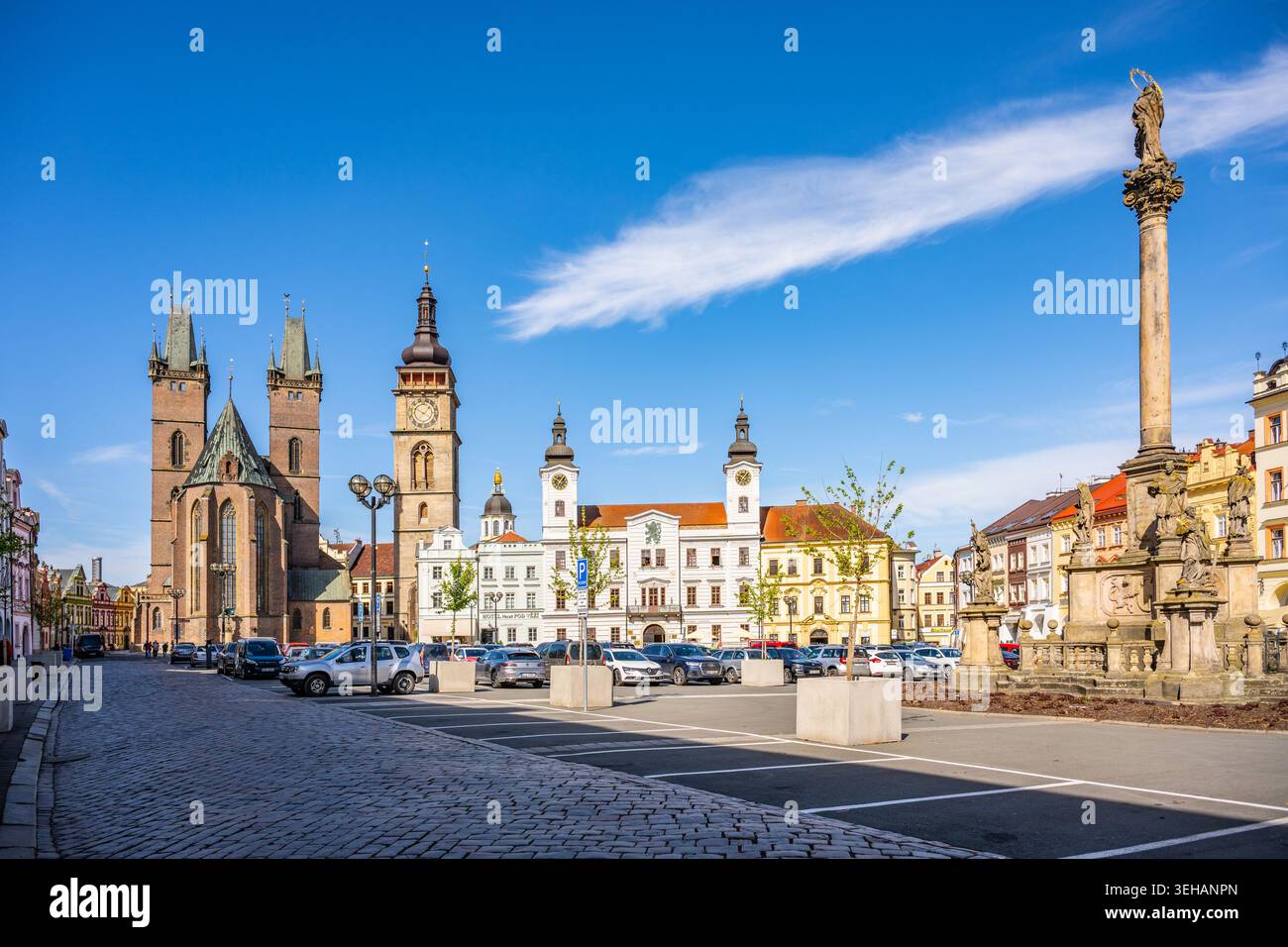 La gente cammina nella grande Piazza di Hradec Kralove. La Cattedrale dello Spirito Santo e la Torre Bianca sono alte. Le auto sono parcheggiate nelle vicinanze. Cielo limpido di Foto Stock