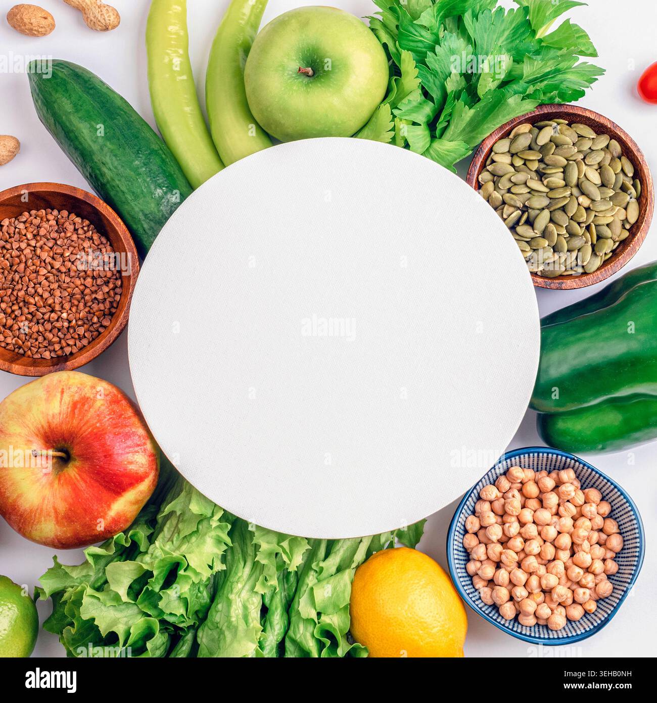 Frutta, verdura, frutta secca e semi verdi sani disposti intorno a un posto bianco vuoto su sfondo bianco. Concetto di dieta bilanciata e spazio di copia per la guarigione Foto Stock