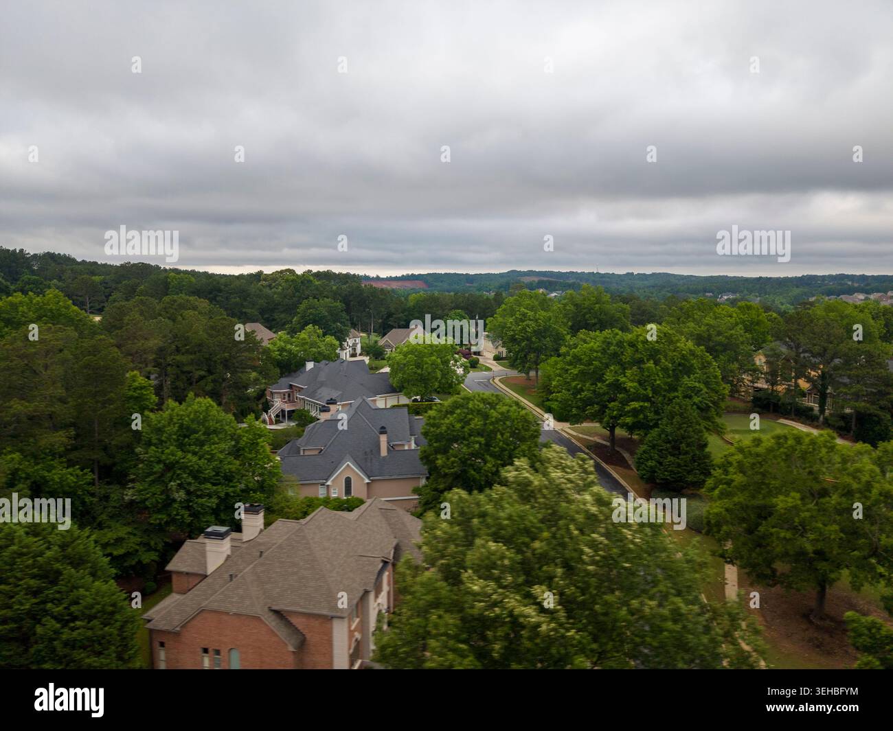 Vista a volo d'uccello di un quartiere residenziale di lusso e di tortuose strade asfaltate delimitate da lussureggianti alberi verdi e proprietà di lusso in un giorno coperto. Foto Stock