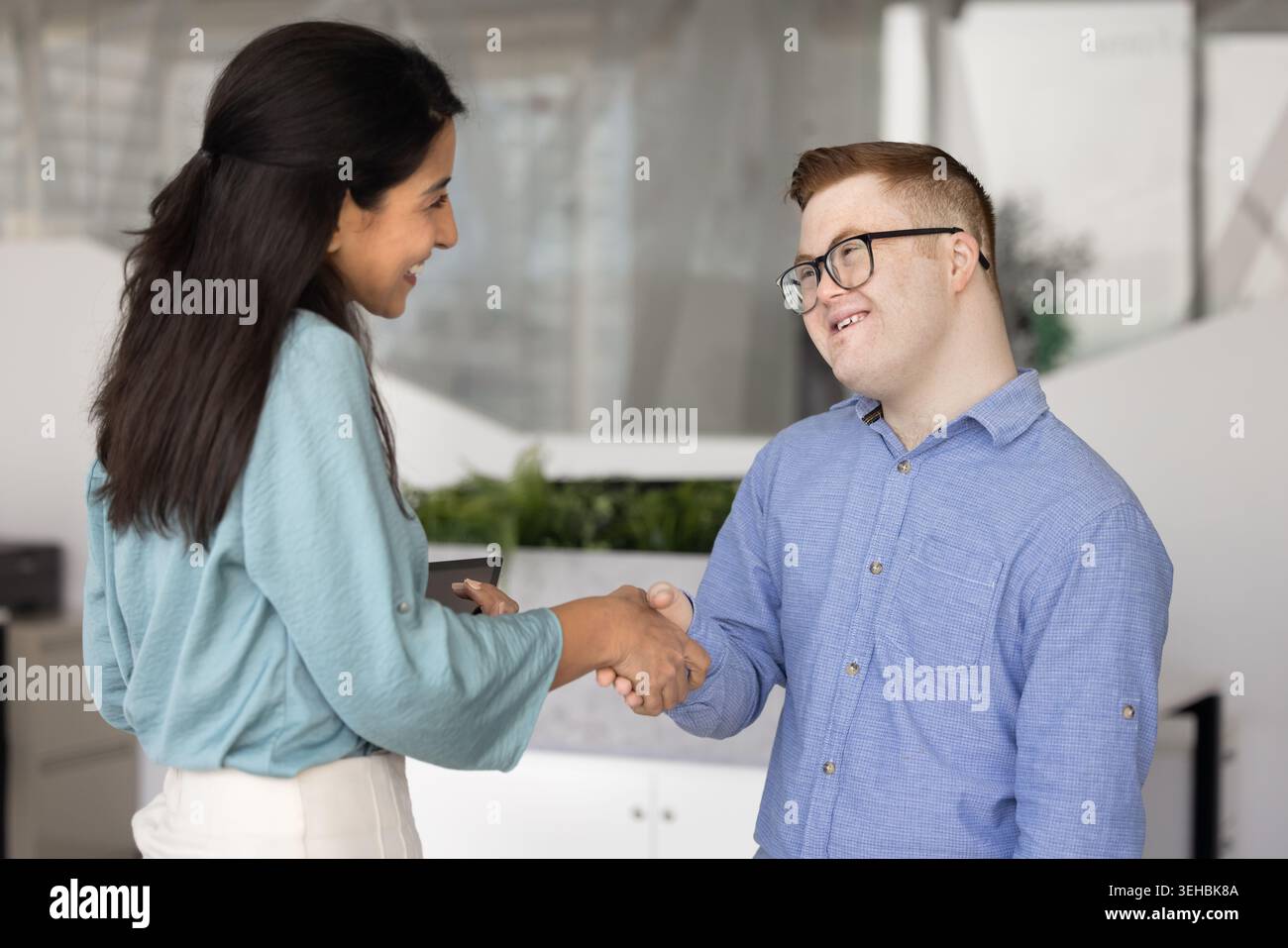 Donna d'affari sorridente che stringe la mano a un uomo con la sindrome di Down Foto Stock