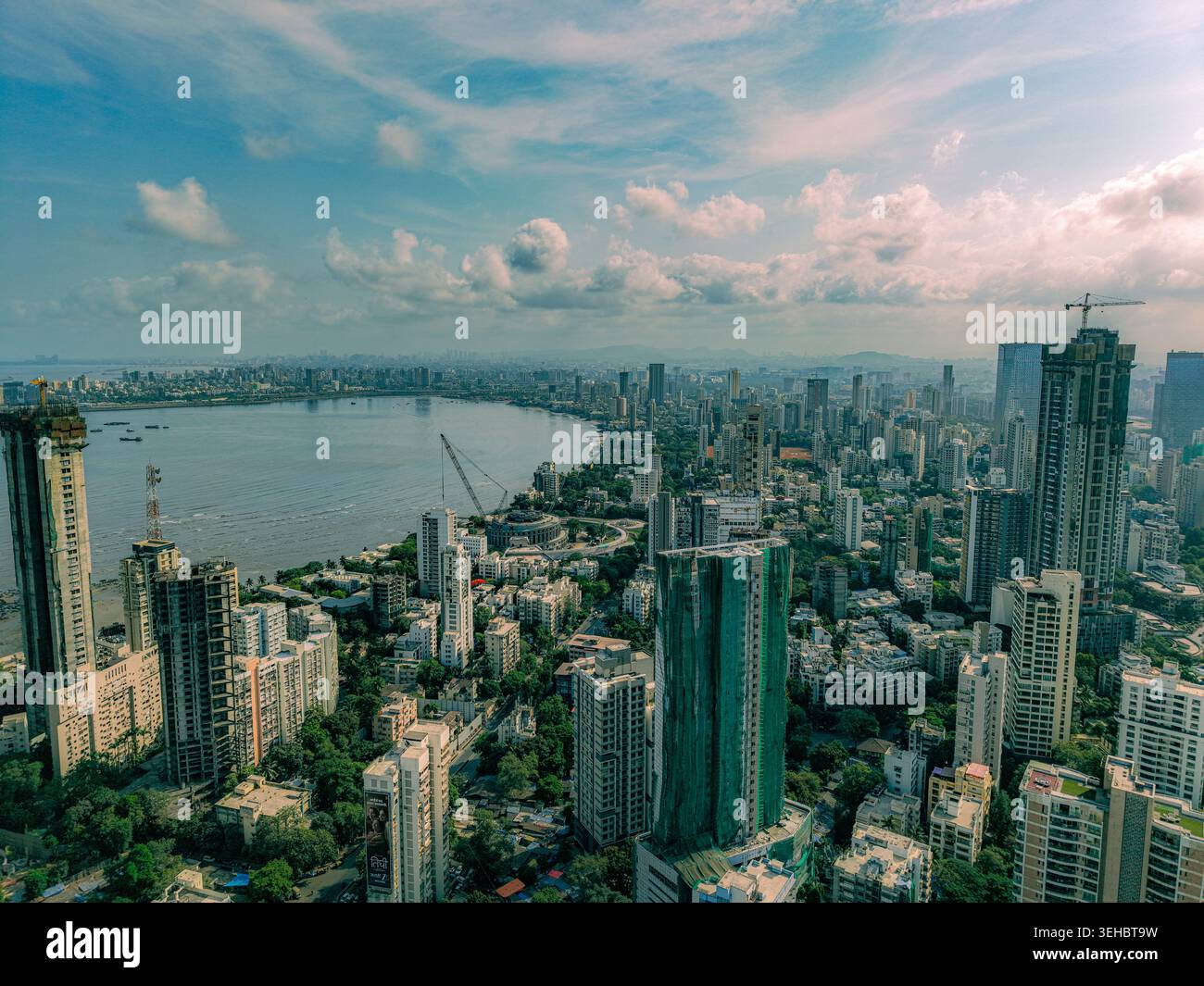Mumbai, India - 17 maggio 2026: Vista aerea del denso skyline urbano con grattacieli e cantieri lungo la baia costiera sotto una nuvolosa Foto Stock