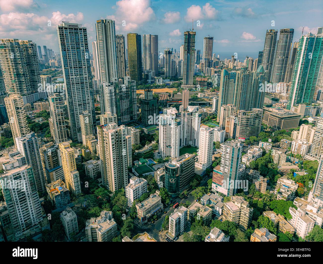 Mumbai, India - 17 maggio 2026: Veduta aerea del denso skyline caratterizzato da grattacieli moderni, grattacieli residenziali e vegetazione urbana sotto una luce luminosa Foto Stock