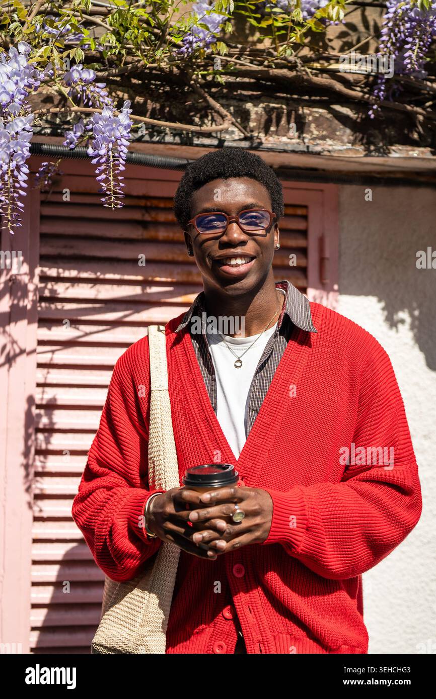 Studente afroamericano alla moda positivo che posa all'aperto in città sorridente alla macchina fotografica Foto Stock