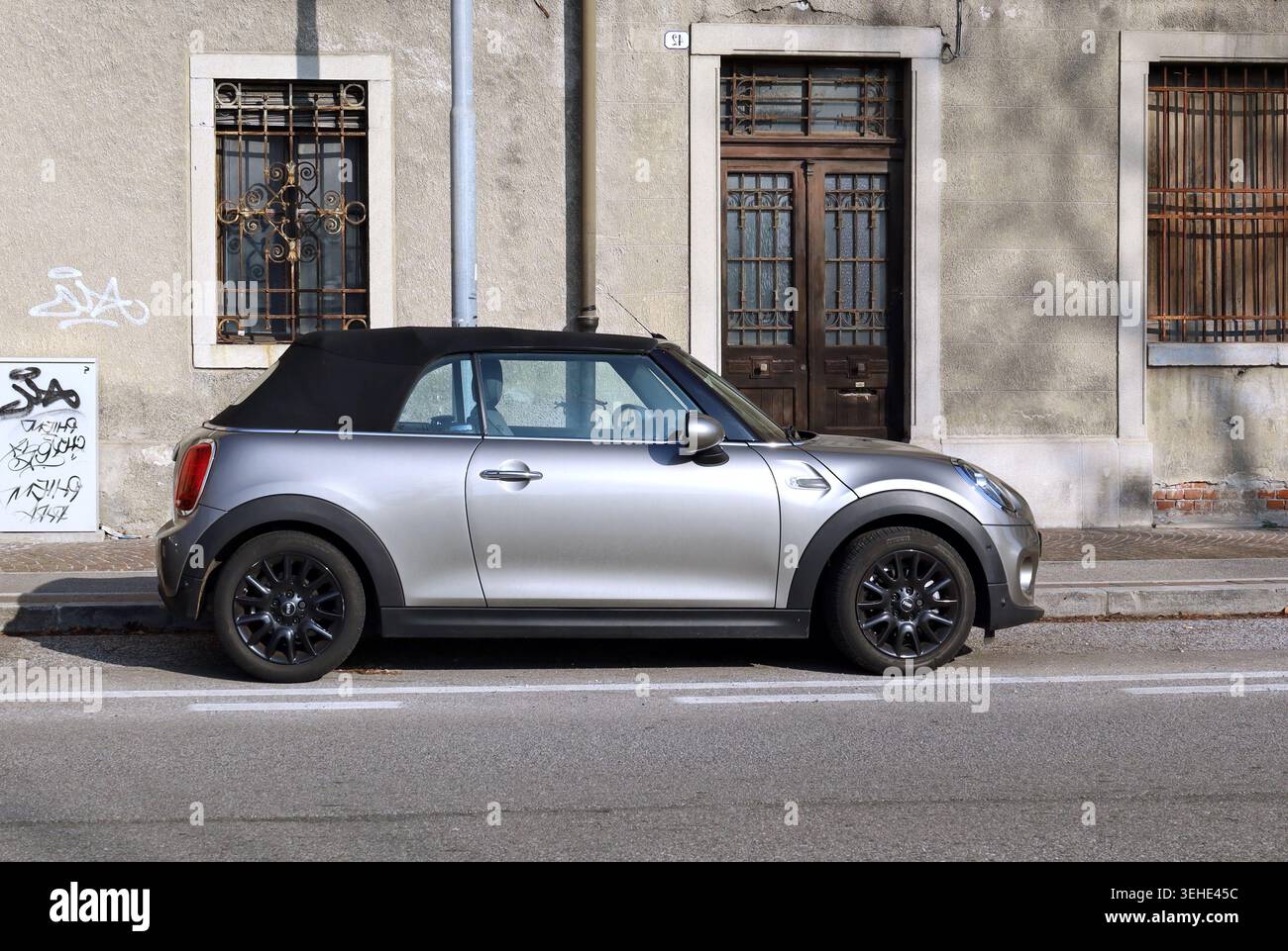 Udine, Italia. 4 febbraio 2023. Mini Cooper grigia convertibile in una strada cittadina con una vecchia casa abbandonata sullo sfondo Foto Stock