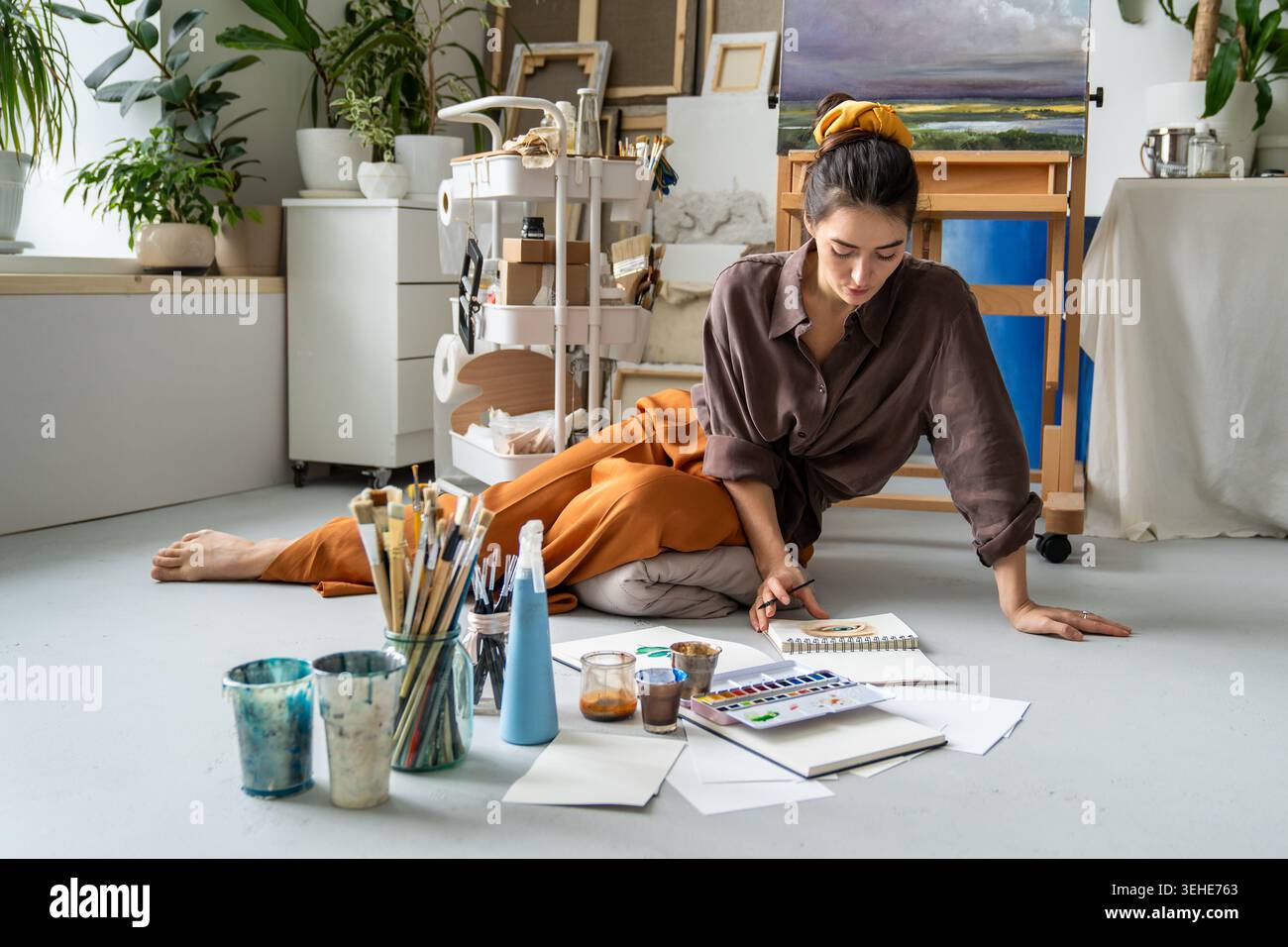 Artista donna spensierata, focalizzata sul disegno di schizzi in un libro di schizzi con acquerello in casa studio. Foto Stock