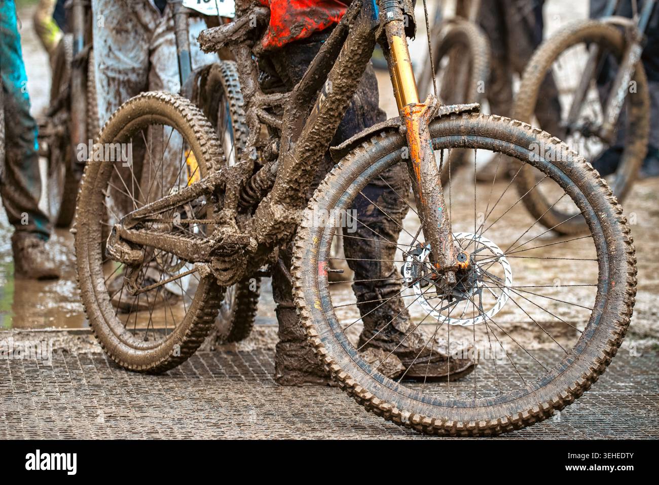 Mountain bike in discesa coperta di fango e ciclista dopo una gara estrema in condizioni di bagnato, mostrando adrenalina, resistenza e un'atmosfera da ciclismo all'aperto Foto Stock