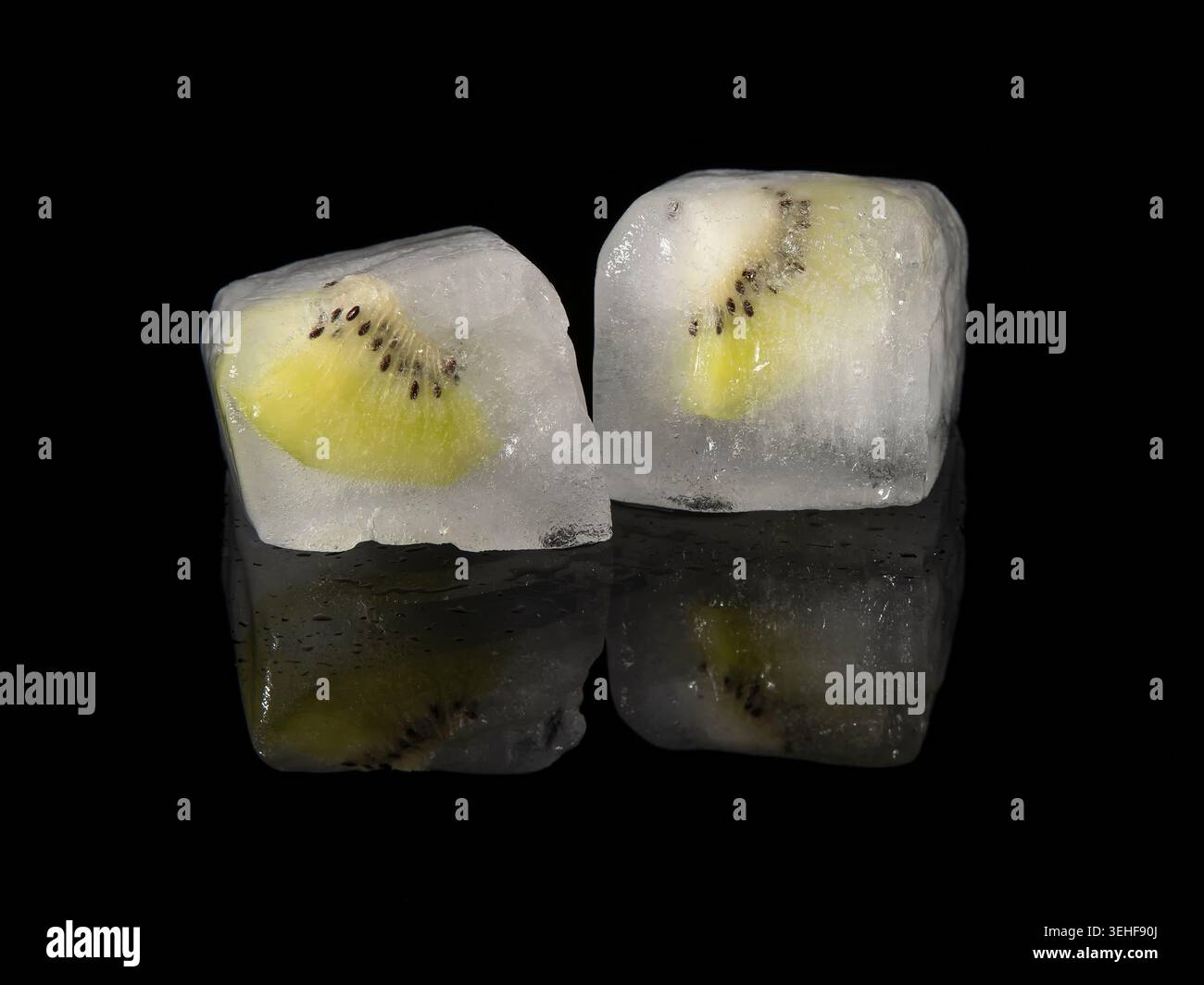 Le fette di Kiwi sono state congelate all'interno di due cubetti di ghiaccio, su uno sfondo nero riflettente Foto Stock