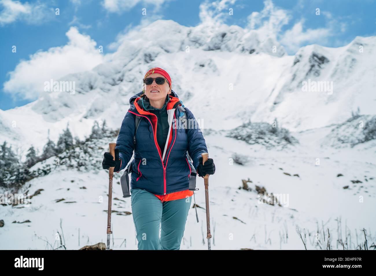 Arrampicatrice con pali da trekking e zaino sotto la montagna Eisenerzer Reichenstein in Austria, che rappresenta l'alpinismo invernale gli sport estremi all'aperto Foto Stock
