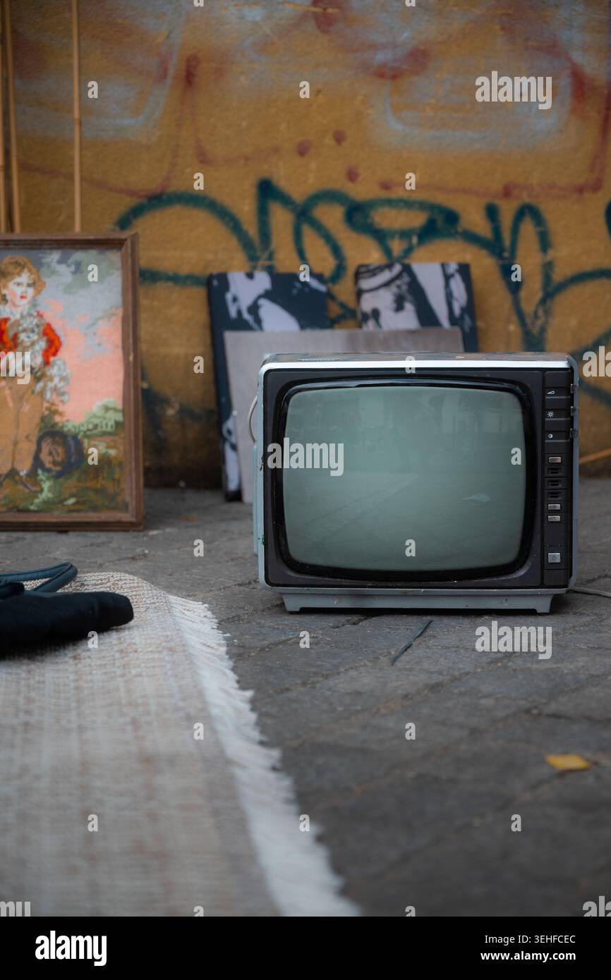 Televisore d'epoca sul marciapiede accanto a dipinti incorniciati e muratura di graffiti, mercato delle pulci porte de Clignancourt, Parigi, Francia. Foto Stock