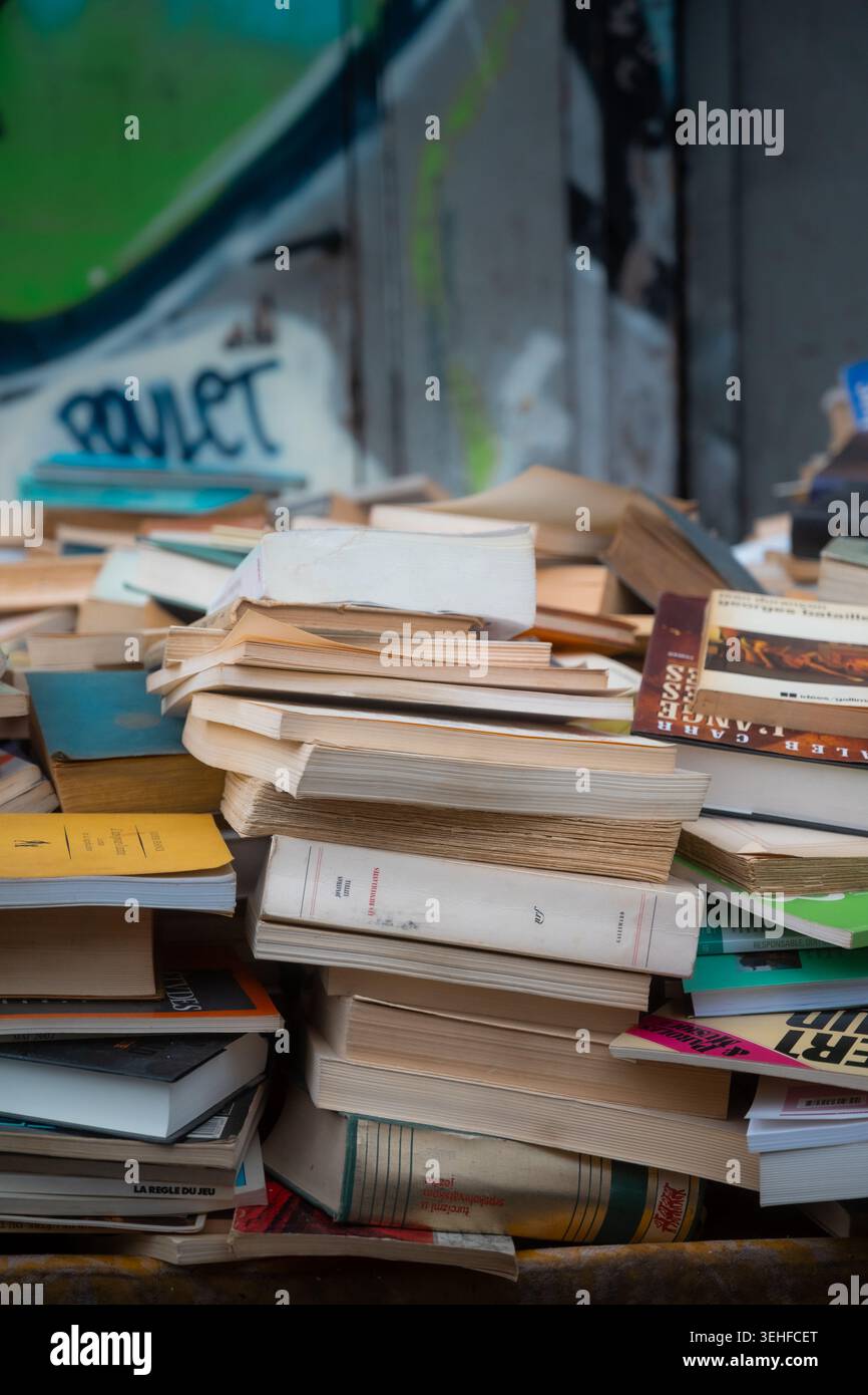 Torreggianti pile di libri di seconda mano contro un muro di graffiti al mercato delle pulci porte de Clignancourt, Saint-Ouen, Parigi, Francia, primavera 2026. Foto Stock