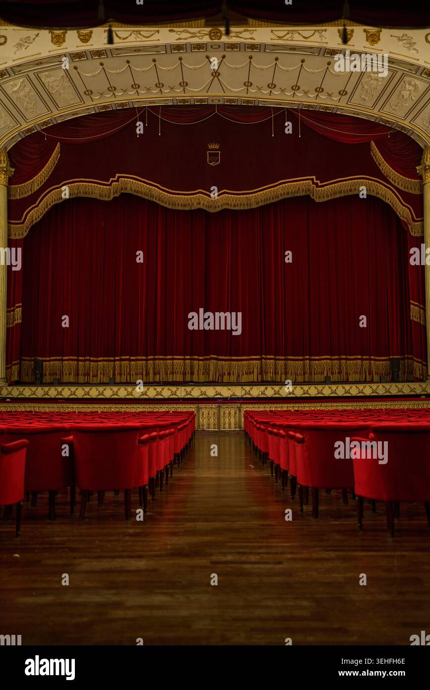 Teatro classico con tende chiuse in velluto rosso e file di posti rossi vuoti, in attesa di uno spettacolo Foto Stock