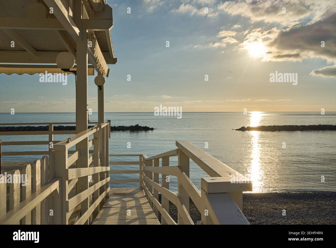 Passerella bianca in legno che si affaccia sulle calme acque dell'oceano durante un vibrante tramonto, creando un'atmosfera serena e riflettente Foto Stock