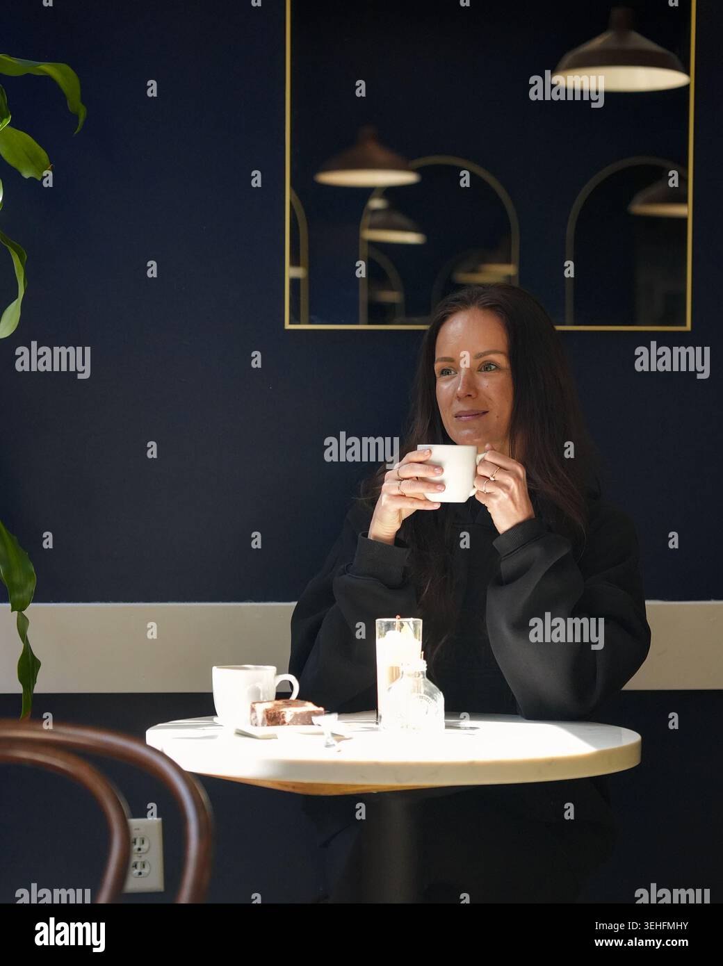 Una giovane donna beve caffè in un moderno bar interno Foto Stock