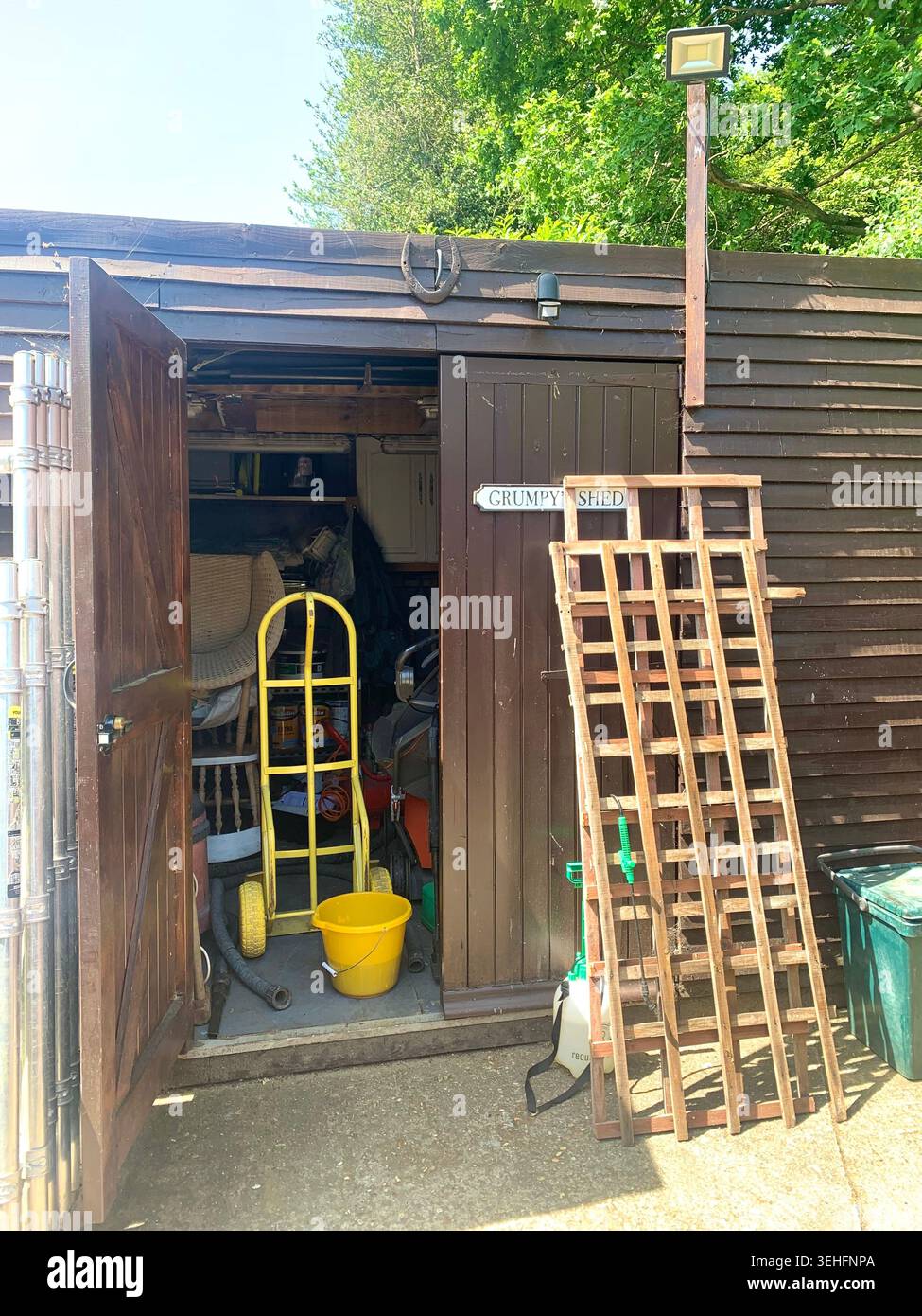 Affascinante casa di periferia con dettagli in stile Tudor e finestre a bovindo bagnate dal giardino estivo alla luce del sole che gettano un prato verde con prato affollato - Immagine stock catturata con smartphone