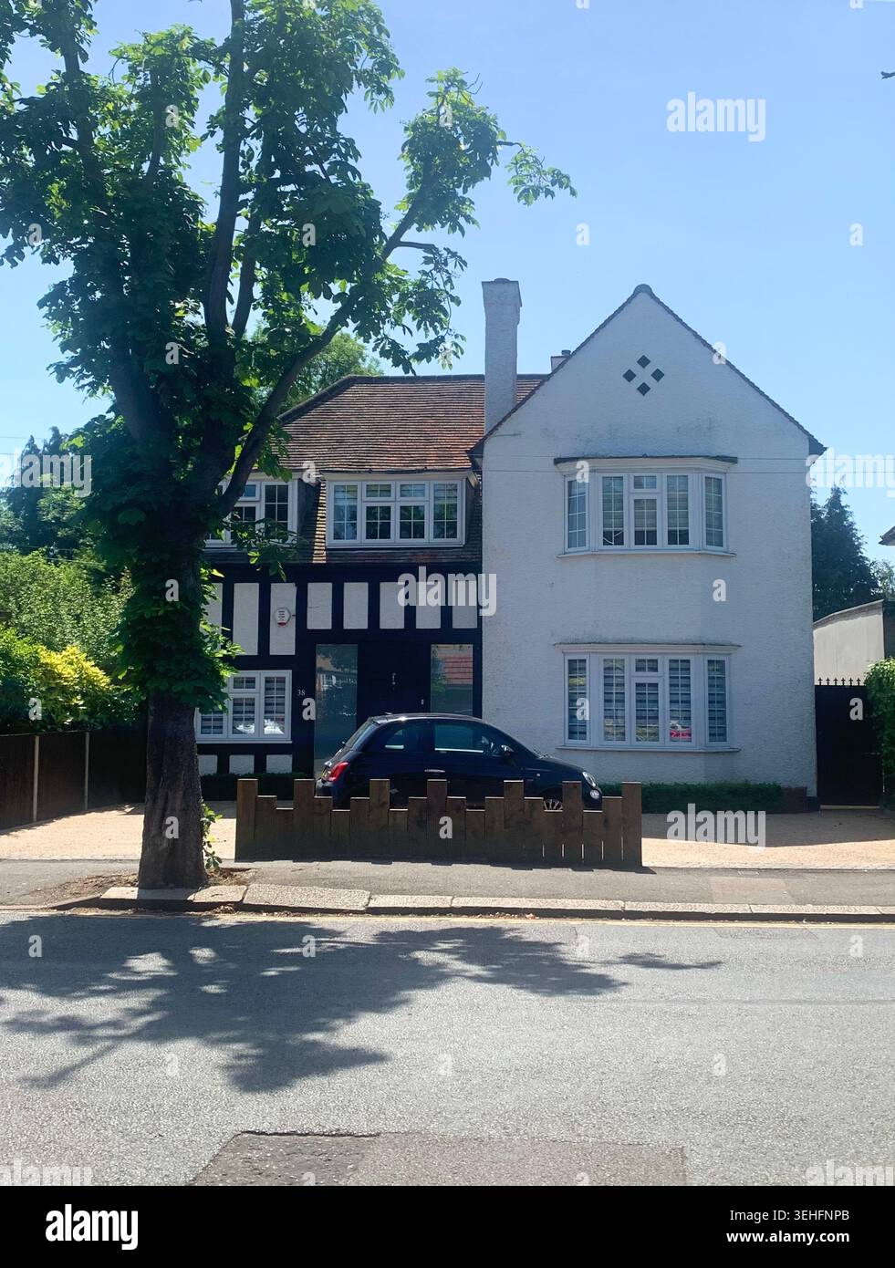Affascinante casa di periferia con dettagli in stile Tudor e finestre a bovindo bagnate dal giardino estivo alla luce del sole che gettano un prato verde con prato affollato - Immagine stock catturata con smartphone