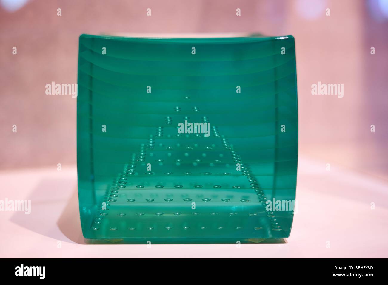 Un pezzo d'arte rettangolare curvo in vetro o acrilico verde trasparente con piccole bolle o punti incastonati disposti in un motivo geometrico triangolare Foto Stock