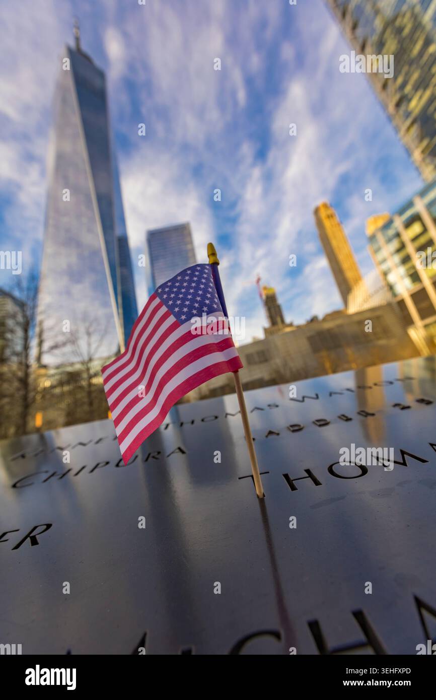 New York City, Stati Uniti - 11 aprile 2026: Una piccola bandiera americana si erge all'interno di un nome inciso sul parapetto di bronzo del National Sep Foto Stock