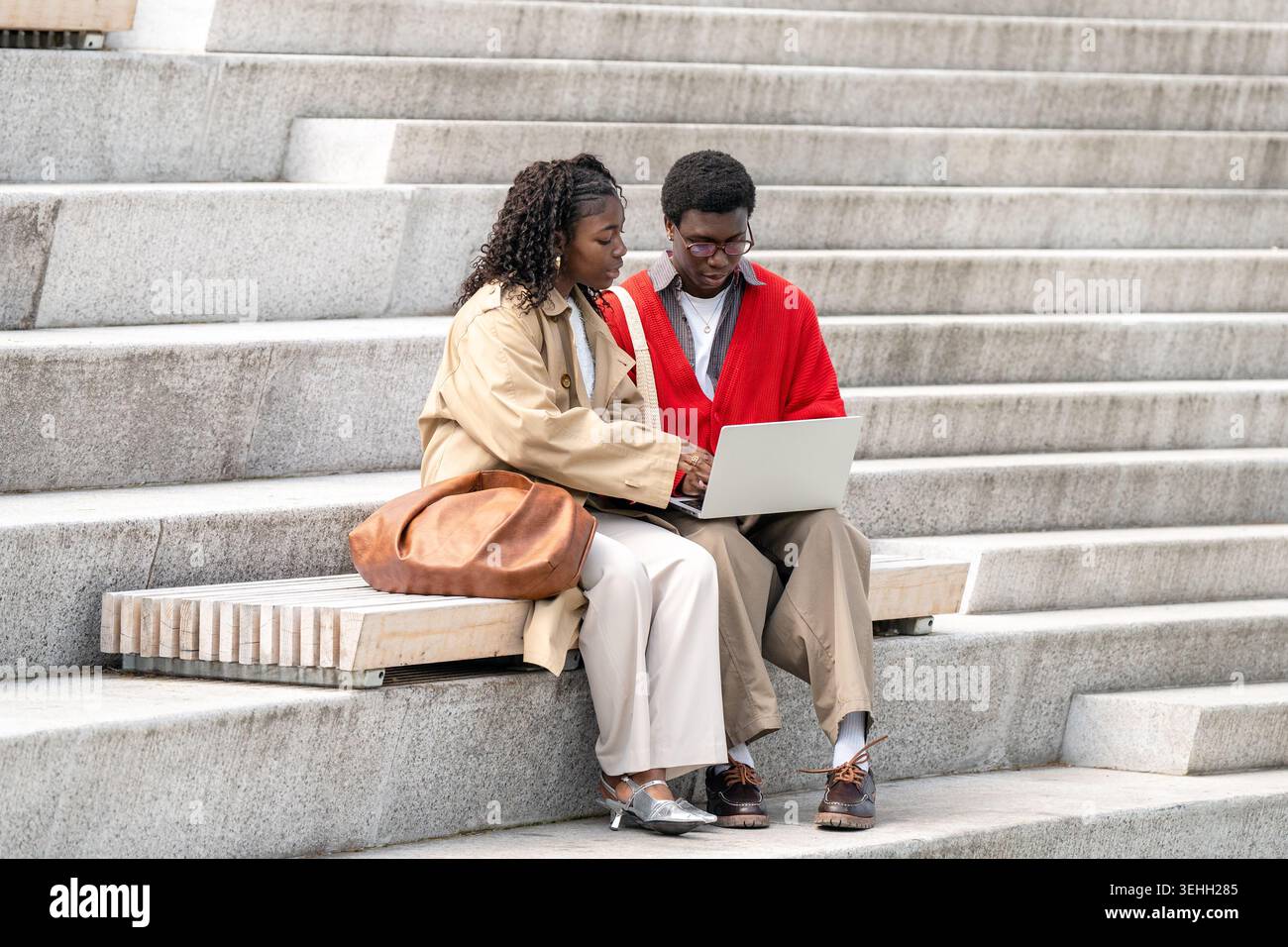 Uno studente di nero incentrato sul nerd spiega gli studi sul laptop a un amico di donna nera seduto all'aperto. Foto Stock
