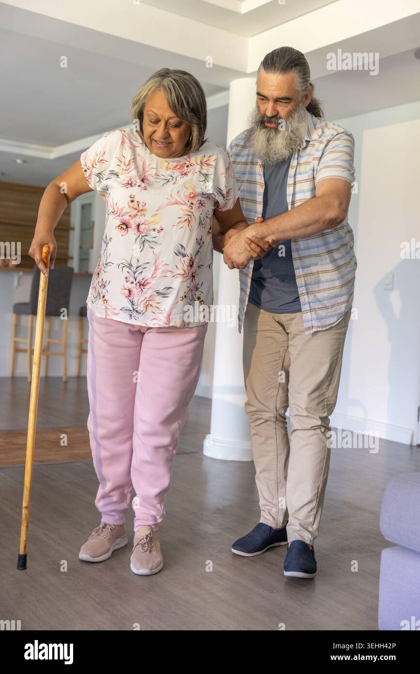 Donna anziana e uomo che cammina a casa, donna in camicetta floreale con sudori rosa che reggono il bastone di legno Foto Stock