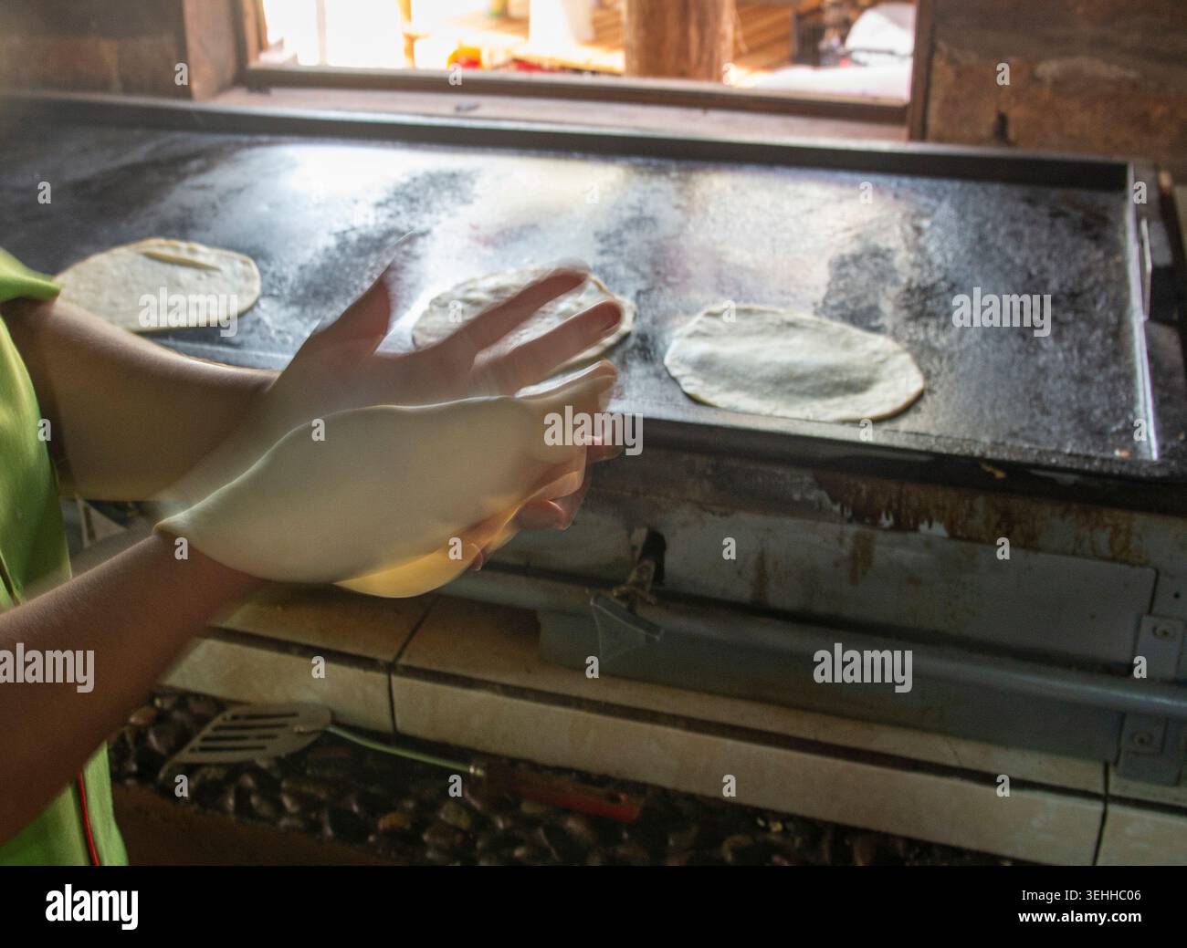 Manipolazione del cibo, le mani di una donna messicana che fa tortillas di farina in una città del Messico su una piastra accanto a una finestra, a Baja California Sur. Foto Stock