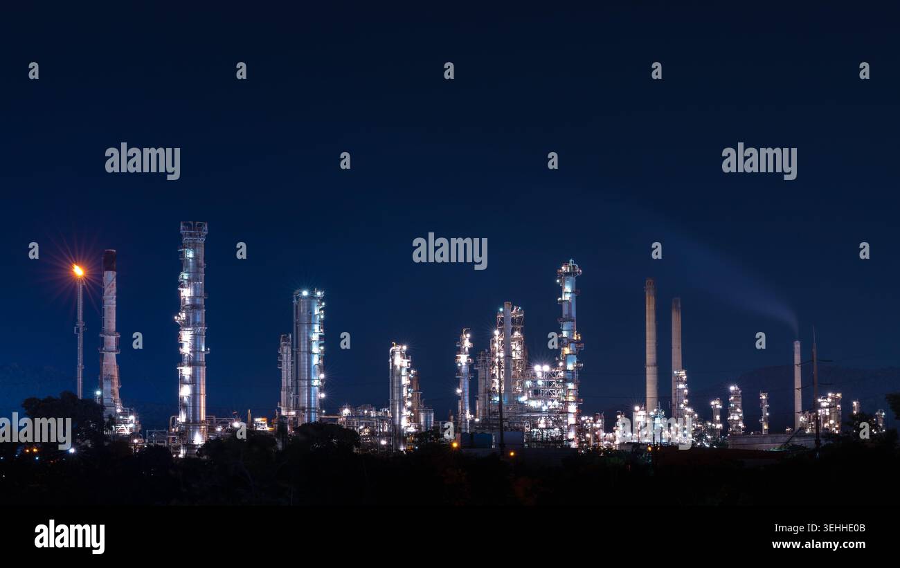 Vista notturna di un impianto petrolchimico con torri faro illuminate e lampi a gas che mettono in risalto le infrastrutture del settore energetico. Foto Stock