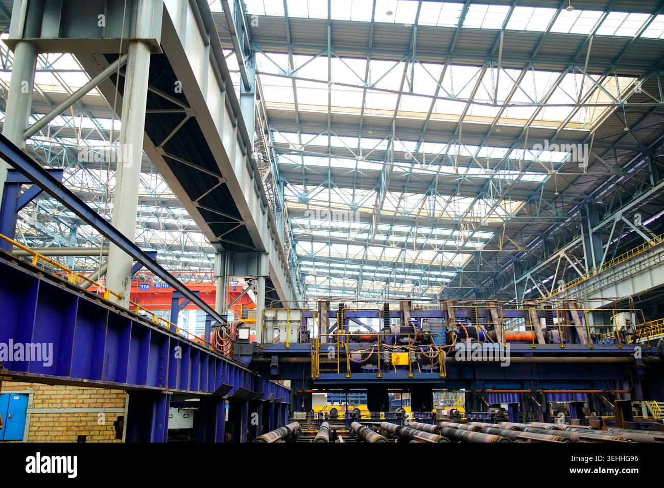 L'area di produzione principale di laminatoio a caldo, l'array di motori di azionamento blu e la tavola dei rulli di laminazione arrugginiti costituiscono l'officina industriale di formalina in acciaio Foto Stock
