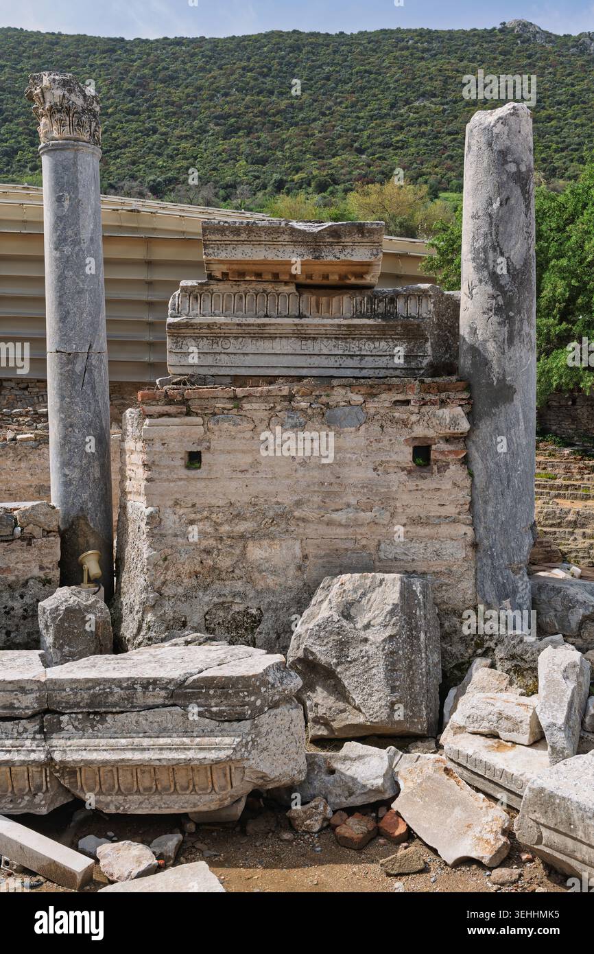 Antiche rovine di Efeso con una colonna corinzia, blocchi di pietra scolpiti con iscrizioni e una collina verde. Selcuk, Turchia Foto Stock