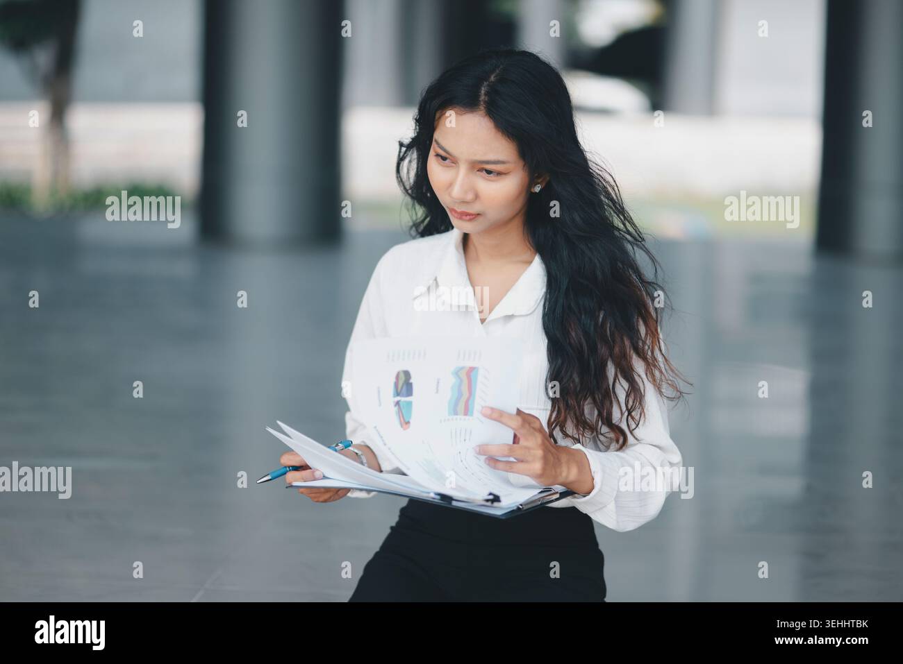 Donna d'affari concentrata che tiene grafici e documenti su una lavagna, ideale per reportistica finanziaria, revisione delle prestazioni, pensiero strategico, professionale Foto Stock
