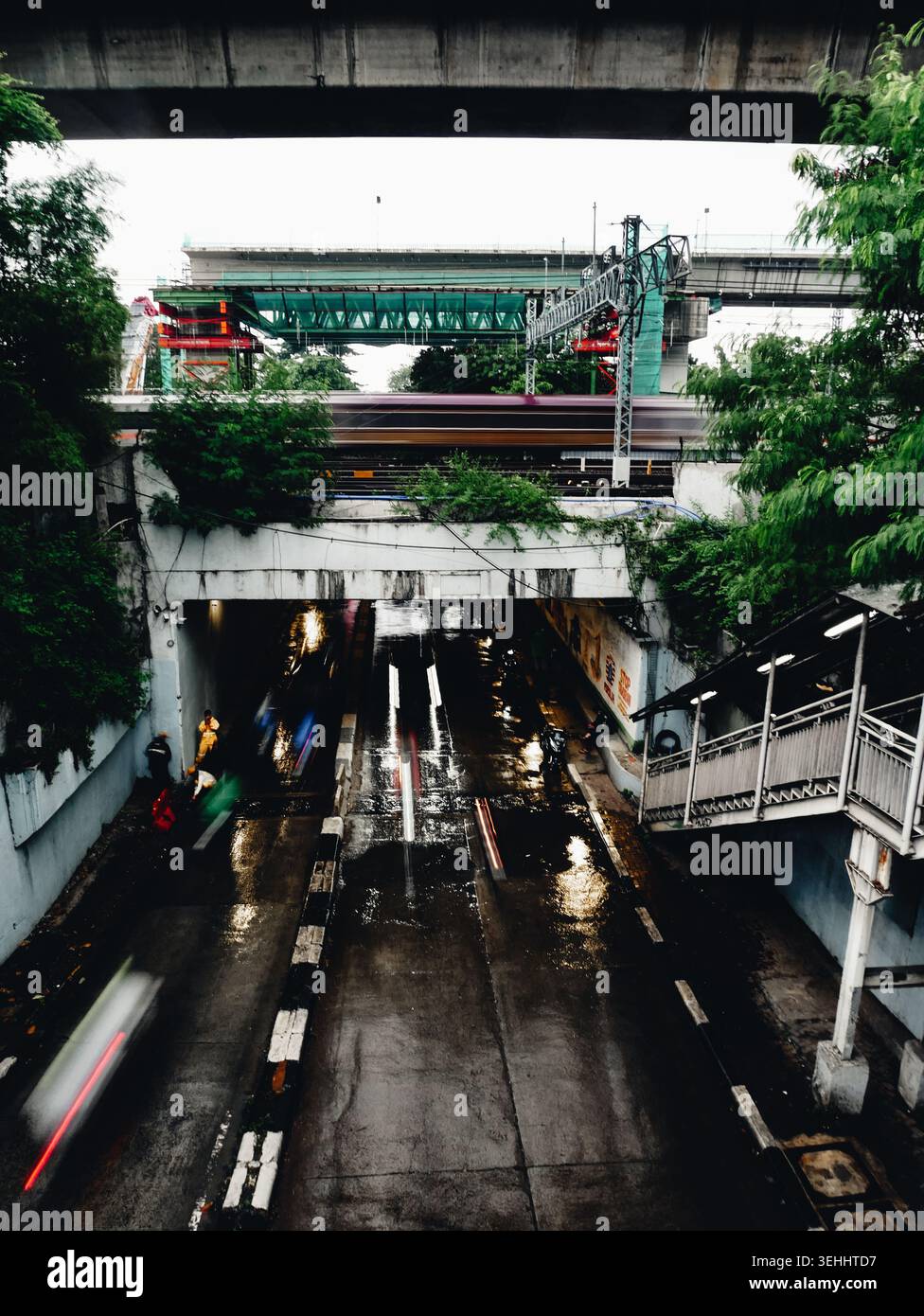 Una vista dal ponte pedonale della stazione Manggarai di Giacarta Indonesia durante il giorno di pioggia, mostrando auto, moto e treno che passano Foto Stock