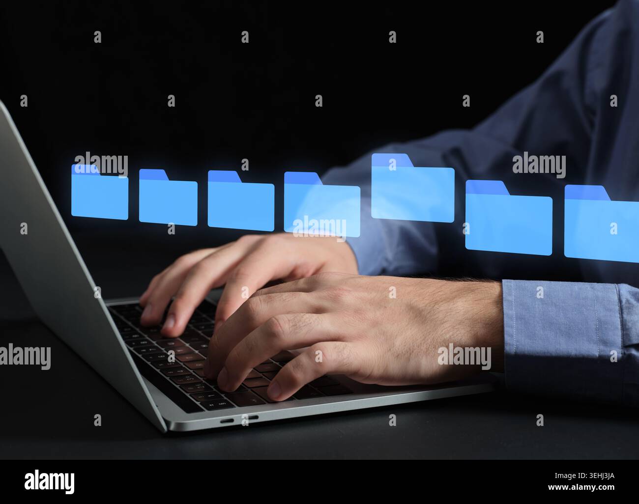 Le mani di una persona scrivono su un laptop con icone olografiche delle cartelle che rappresentano i dati digitali o la gestione delle risorse digitali e lo storage su cloud Foto Stock