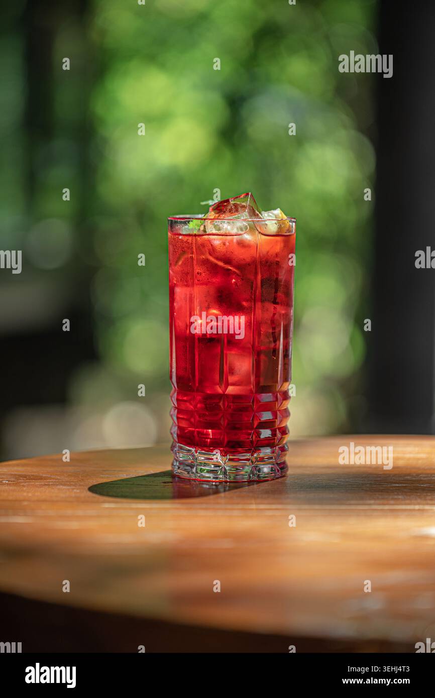 Cocktail rosso con ghiaccio sul tavolo di legno Foto Stock