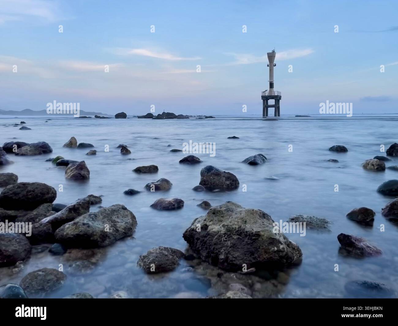 Un paesaggio panoramico a lunga esposizione di Pidakan Beach a Pacitan, Giava orientale, caratterizzato da una torre faro al largo bianco che sorge nell'oceano circondato - Immagine stock catturata con smartphone