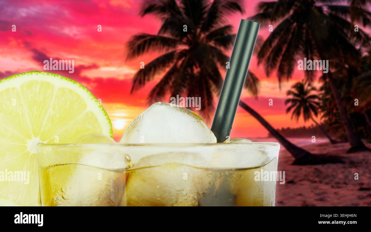 Un cocktail rinfrescante con cubetti di ghiaccio e una fetta di lime, sullo sfondo di una spiaggia tropicale al tramonto Foto Stock