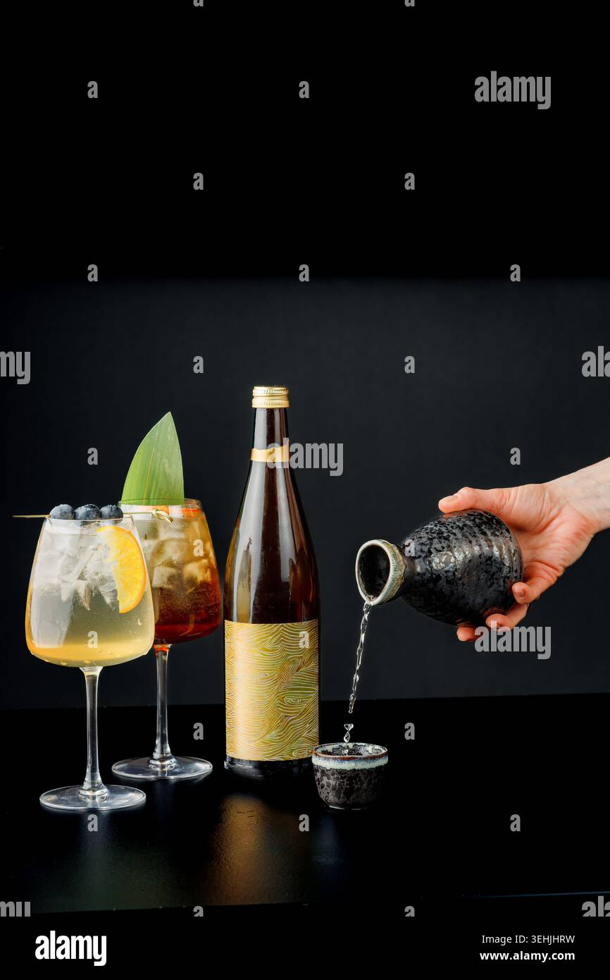 Uomo che versa la bevanda nel bicchiere accanto alla bottiglia e ai cocktail. Luce da studio, composizione professionale. Spazio per il testo Foto Stock
