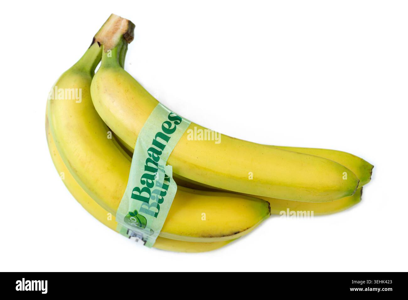 Un gruppo di banane gialle è tenuto insieme da un'etichetta adesiva verde su sfondo bianco. Foto Stock