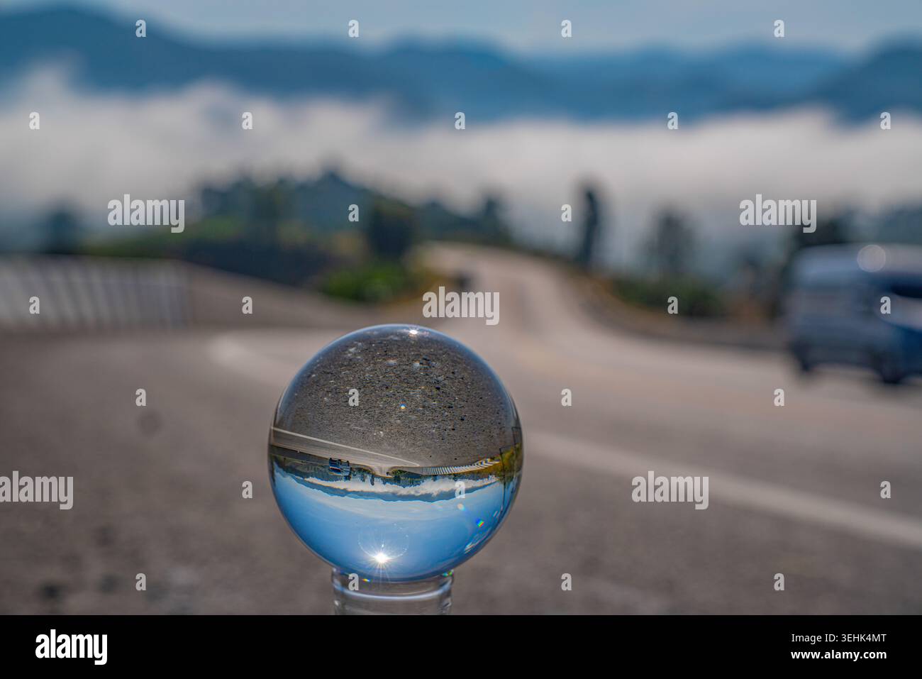 Una limpida sfera di cristallo cattura un riflesso invertito di un paesaggio sereno con cielo blu e montagne lontane, creando un perspe surreale e artistico Foto Stock