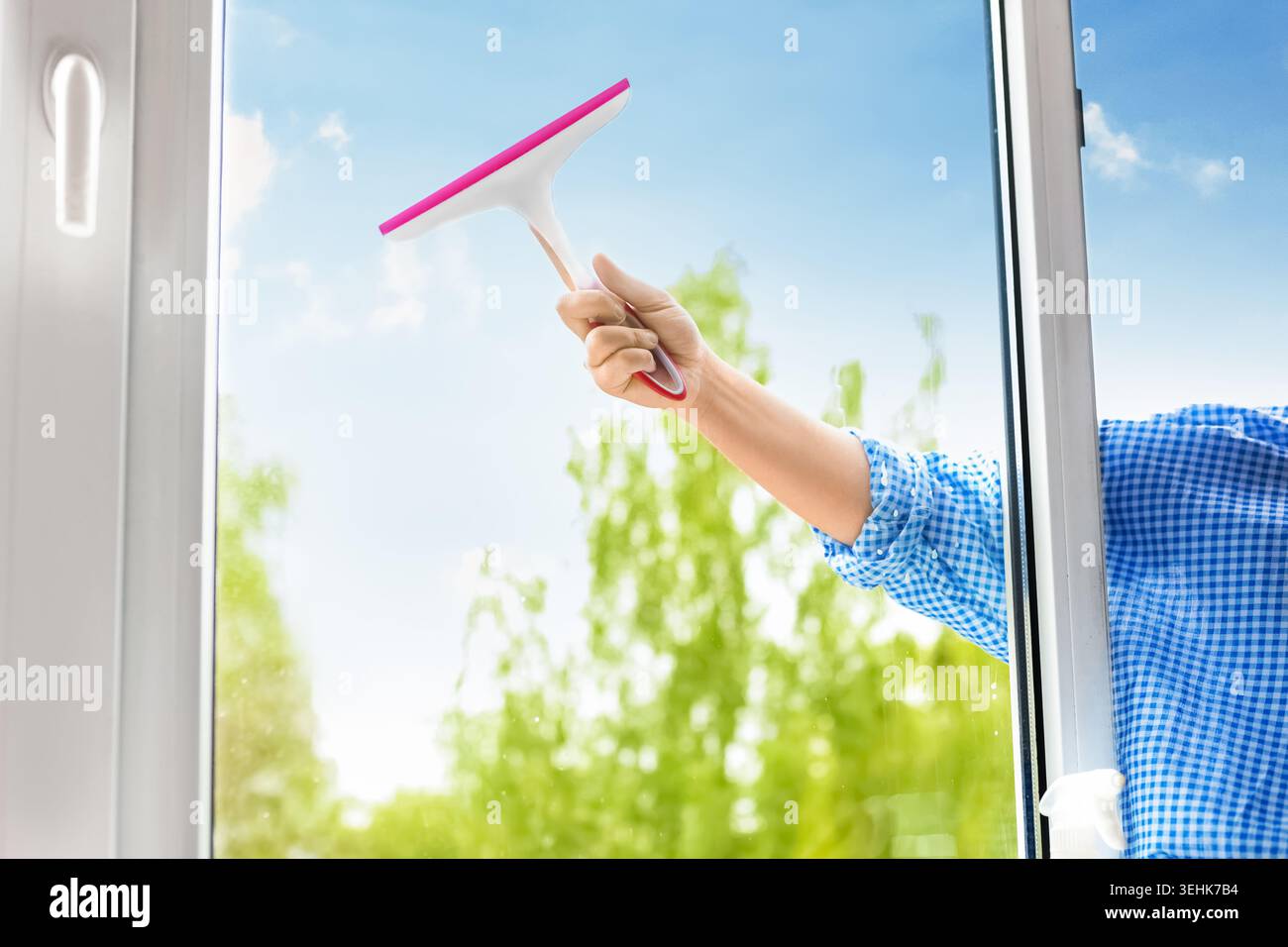 Primo piano di una lavatrice a mano con una spatola contro un cielo azzurro e luminoso e alberi verdi. Ideale per le pulizie primaverili e le faccende domestiche Foto Stock