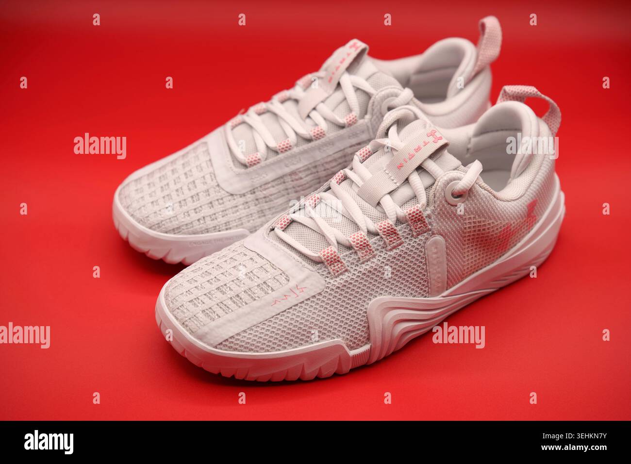 Un paio di sneaker da training Under Armour TriBase Reign 6 bianche e rosa chiaro con un solido sfondo rosso brillante Foto Stock